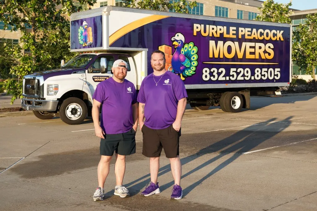 Derik and Chris, owners of Purple Peacock Movers, standing in front of their purple moving truck